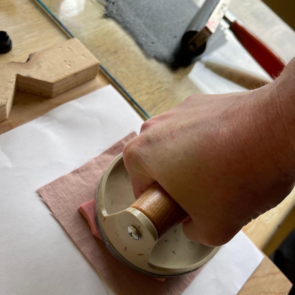 a hand pressing a baren onto a block pressing ink onto a piece of linen